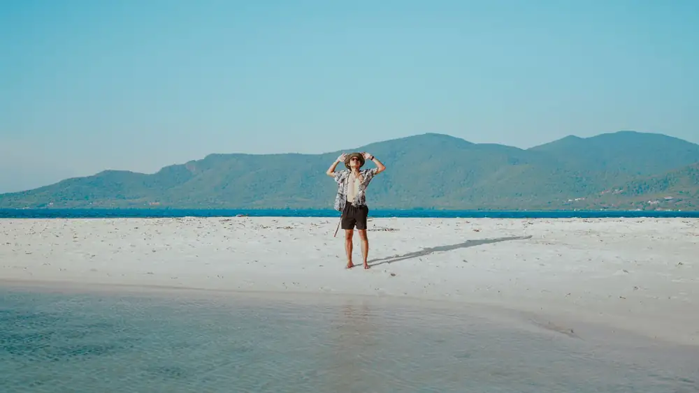 Young man enjoying a sunny day on a serene tropical beach with mountain views.