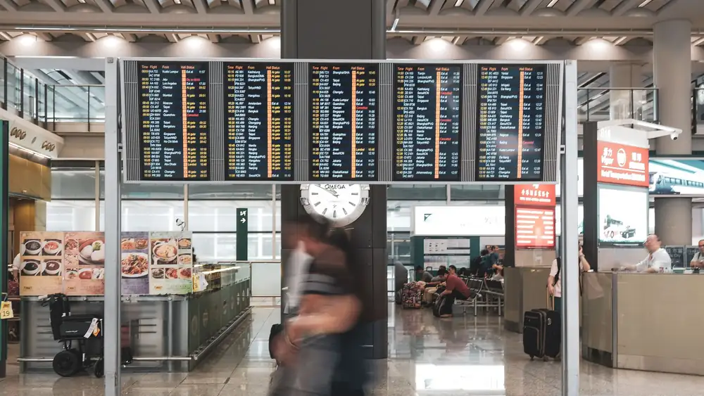 Blurred motion of travelers in a modern airport terminal with departure screens and a prominent clock.