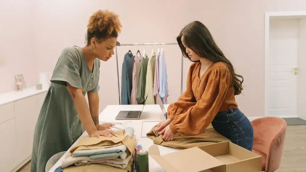Two young women working together in a modern boutique, organizing clothes with focus and style.