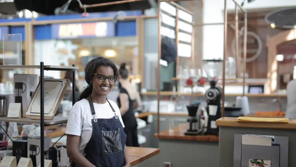 Smiling barista standing in a stylish café, showcasing entrepreneurial spirit.