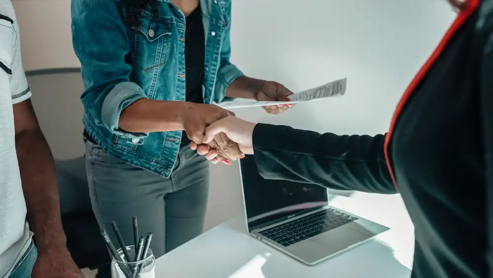 Two people shaking hands over a desk signifies a business agreement or partnership.