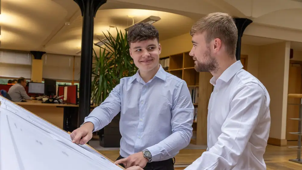 Two young professionals discussing plans in a modern, well-lit office setting.