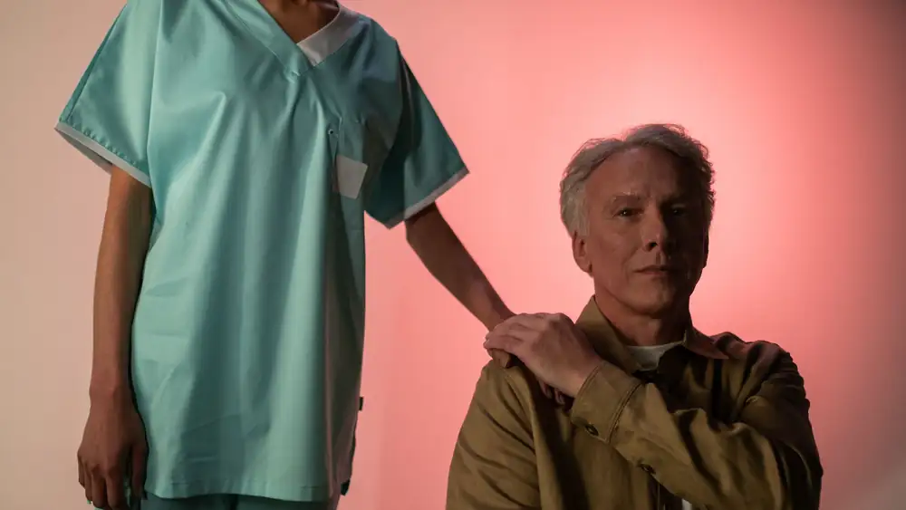 Portrait of an elderly man with a caregiver in medical attire, studio light background.