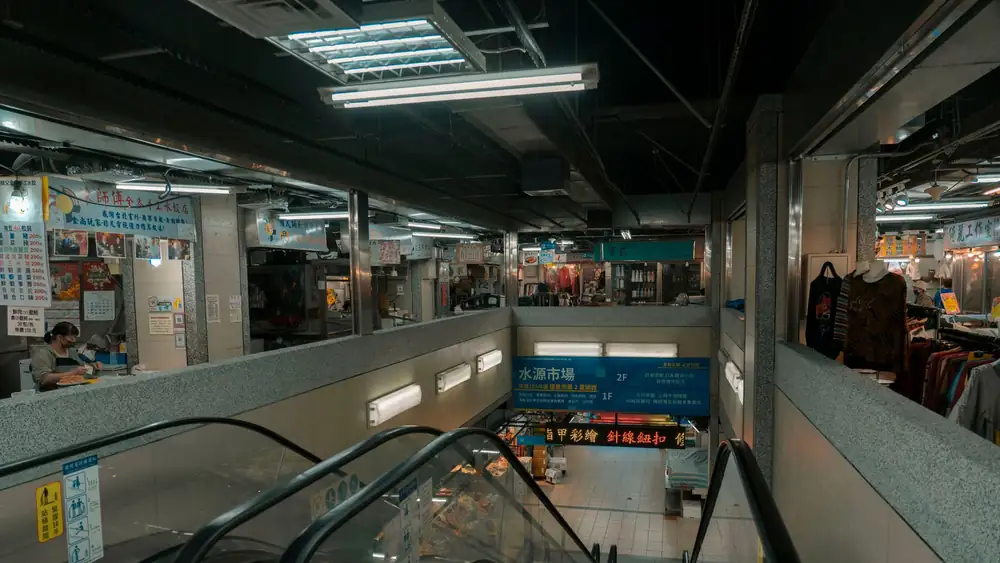 Interior view of a modern shopping mall with escalators and retail shops.