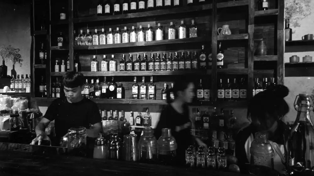 Classic black and white image of bartenders working behind a bar stocked with bottles.