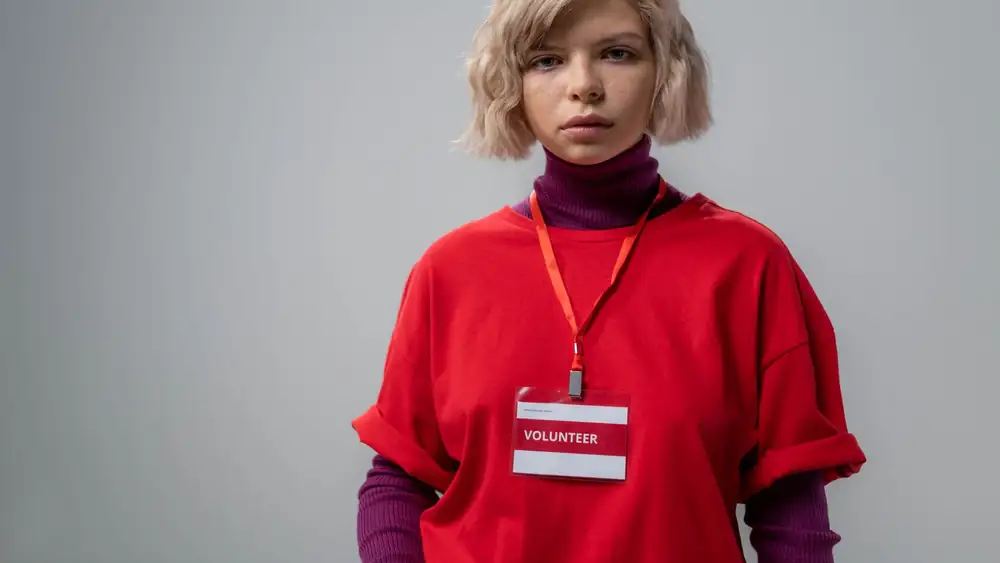 Portrait of a young female volunteer wearing a red shirt and name badge against a neutral background.