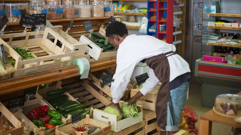 Grocery store worker arranging fresh vegetables in a market display.