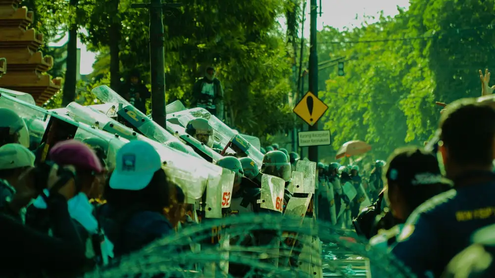 A dynamic scene of people and police during a street protest in a sunny urban area.