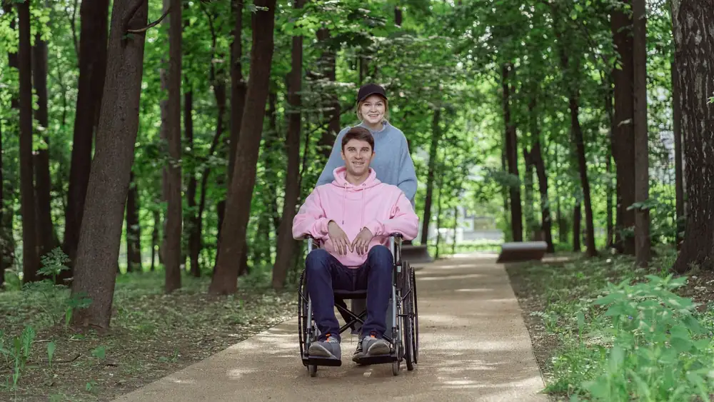 Smiling couple enjoying a sunny day in a park. Man in a wheelchair being pushed by a woman.
