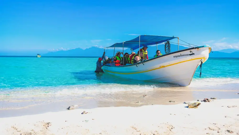 Tourists enjoy a boat ride on a vibrant tropical beach with clear blue waters.