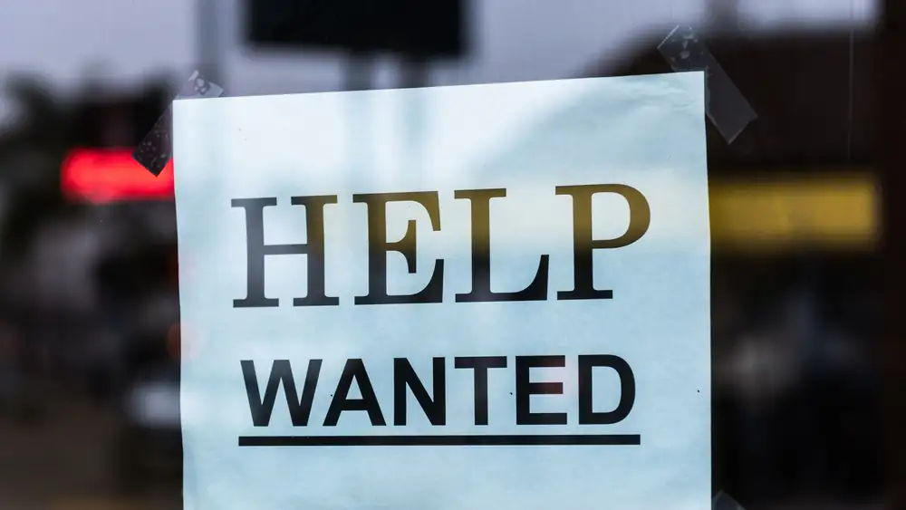 Close-up of a Help Wanted sign taped to a glass window in a storefront.
